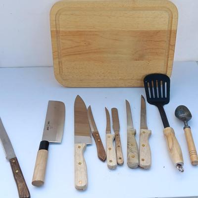 Wooden cutting board with a variety of knives and wood handled utensils.