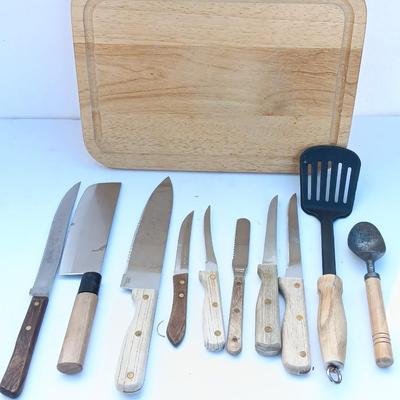 Wooden cutting board with a variety of knives and wood handled utensils.
