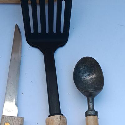 Wooden cutting board with a variety of knives and wood handled utensils.