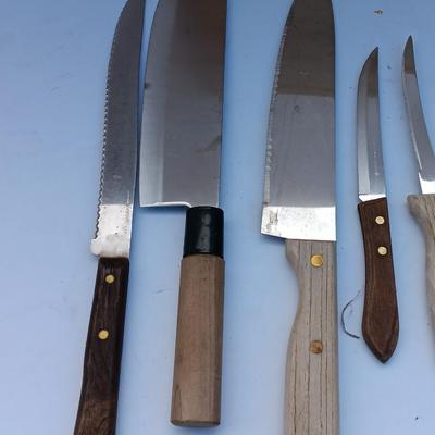 Wooden cutting board with a variety of knives and wood handled utensils.
