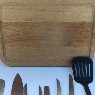Wooden cutting board with a variety of knives and wood handled utensils.