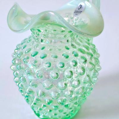 Sale Photo Thumbnail #587: This original green iridescent Fenton jug has its Fenton sticker which is silver and says handmade in USA. This hobnail jug has the Fenton stamp on the bottom. It is iridescent, hob nail and stands a total of 5 inches tall with a ruffled top. It is a beau