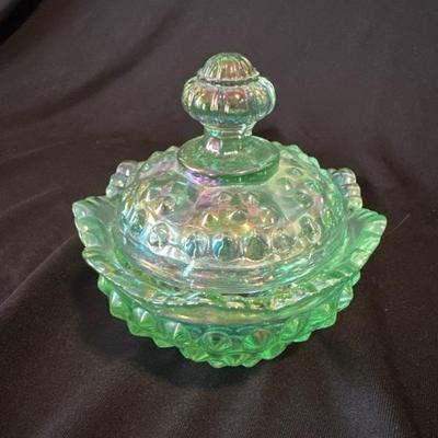 Sale Photo Thumbnail #815: Green iridescent hobnail Fenton bowl with lid, very good condition. Fenton can be seen stamped into the glass on lid and bowl. Sticker on inside.

Approximately 3.5in tall and 3.5in wide