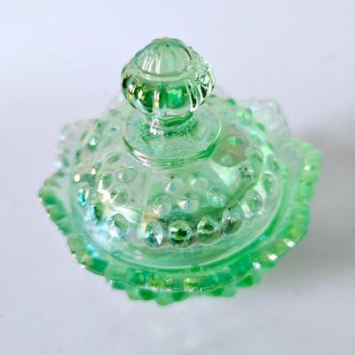 Sale Photo Thumbnail #818: Green iridescent hobnail Fenton bowl with lid, very good condition. Fenton can be seen stamped into the glass on lid and bowl. Sticker on inside.

Approximately 3.5in tall and 3.5in wide