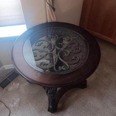 WOOD FRAMED ROUND END TABLE WITH ORNATE METAL CENTER COVERED WITH GLASS