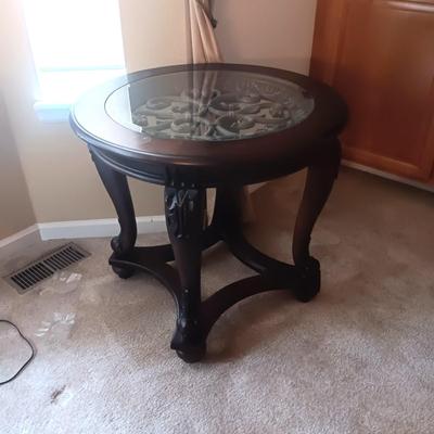WOOD FRAMED ROUND END TABLE WITH ORNATE METAL CENTER COVERED WITH GLASS
