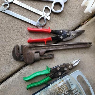 Sale Photo Thumbnail #719: Lot of 2 crescent wrenches, 3 spanner wrenches, left and right snips, pipe wrench, drill bit assortment, metal case now full of bolts, circuit and voltage tester and I have no idea what the chrome and white thing is .
In garage.