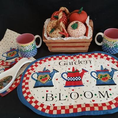 Two Garden Bloom placemats with fabric handmade apples in a basket, and mugs with a spoon rest