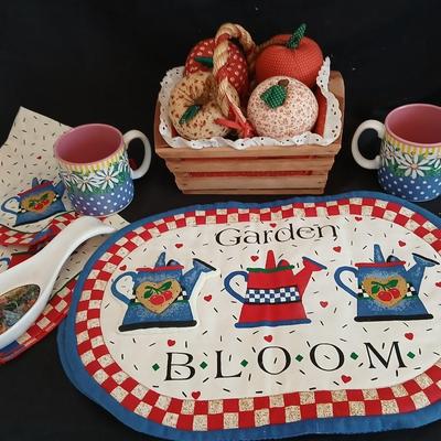Two Garden Bloom placemats with fabric handmade apples in a basket, and mugs with a spoon rest