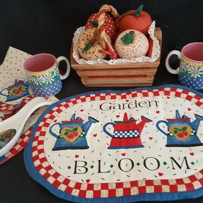 Two Garden Bloom placemats with fabric handmade apples in a basket, and mugs with a spoon rest