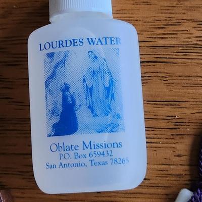 Sale Photo Thumbnail #266: This auction lot is for Lourdes Water and Two Crosses.  The Blessed water is in a small plastic bottle.  One small plastic cross is imprinted with the words - Jesus Cares and has a purple fringe.  The remaining cross is carved wood featuring the head of C