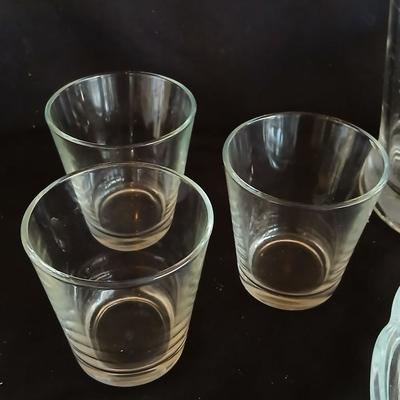Glass water pitcher with six small juice glasses and a snack bowl with a platter