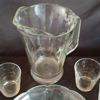 Glass water pitcher with six small juice glasses and a snack bowl with a platter