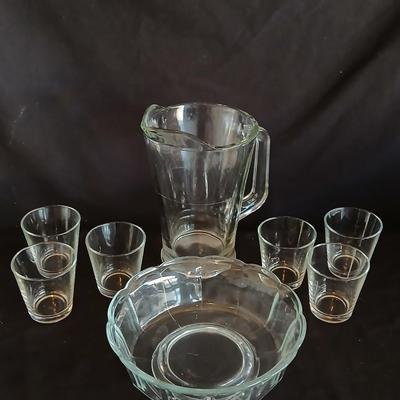 Glass water pitcher with six small juice glasses and a snack bowl with a platter