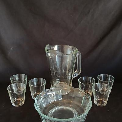 Glass water pitcher with six small juice glasses and a snack bowl with a platter