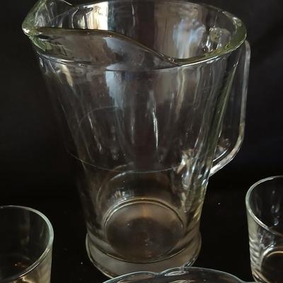 Glass water pitcher with six small juice glasses and a snack bowl with a platter