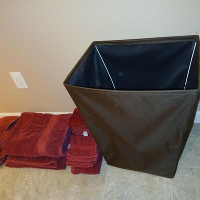Brown laundry hamper with assortment of reddish /maroon towels