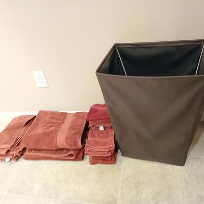Brown laundry hamper with assortment of reddish /maroon towels