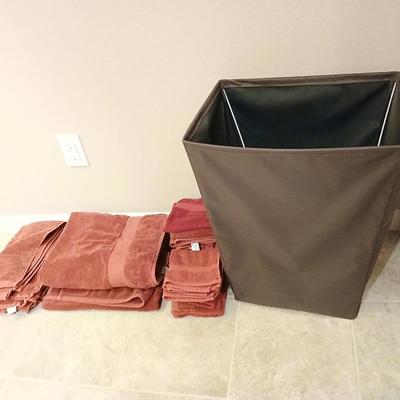 Brown laundry hamper with assortment of reddish /maroon towels