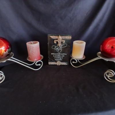 Two metal candle sconces with two candles and two decorative balls and a religious plaque