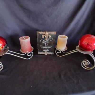 Two metal candle sconces with two candles and two decorative balls and a religious plaque