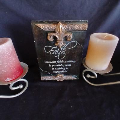 Two metal candle sconces with two candles and two decorative balls and a religious plaque