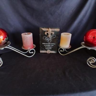 Two metal candle sconces with two candles and two decorative balls and a religious plaque
