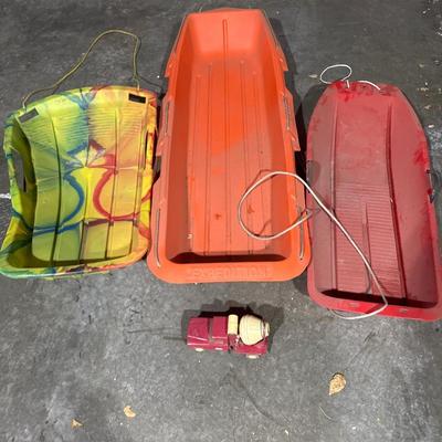 3 plastic sleds and a vintage concrete truck toy.