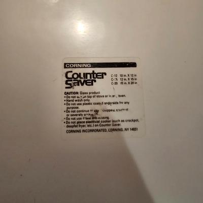 Two corning casserole dishes with lids and a Corning counter cutting board