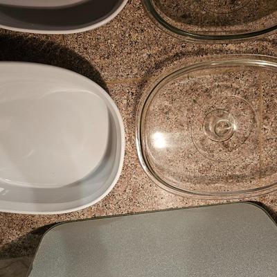 Two corning casserole dishes with lids and a Corning counter cutting board