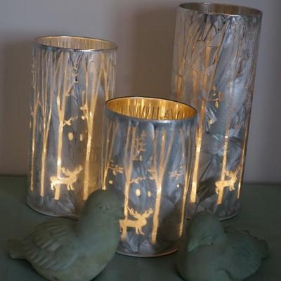 Grouping of three graduated height lanterns, forest trees and antlered deer and birds