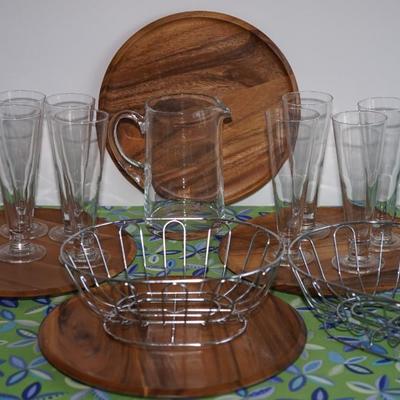 GROUPING OF EIGHT PILSNER GLASSES, TEAK SERVING ROUND TRAYS, TWO HEAVY WIRE SNACK BASKETS