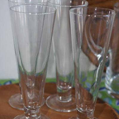 GROUPING OF EIGHT PILSNER GLASSES, TEAK SERVING ROUND TRAYS, TWO HEAVY WIRE SNACK BASKETS