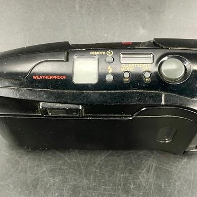 Sale Photo Thumbnail #427: Includes wrist strap and case. Tested with a fresh battery, appears to work as expected.  Good physical condition, no visible damage. Uses 35mm Color film.  Point and shoot style, uses a small viewfinder. LCD digital displays on the top of the camera.