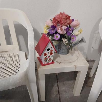 Two heavy duty plastic patio chairs, small table, galvanized watering can with flowers and a birdhouse