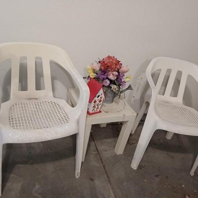 Two heavy duty plastic patio chairs, small table, galvanized watering can with flowers and a birdhouse