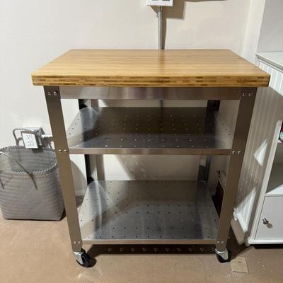 Sale Photo Thumbnail #76: The Nike Kitchen Cart is a modern, rectangular cart designed for kitchen use. It features a combination of stainless steel and bamboo materials, offering a natural finish in a sleek silver color. The cart measures 30 inches in width, 20 inches in depth, a