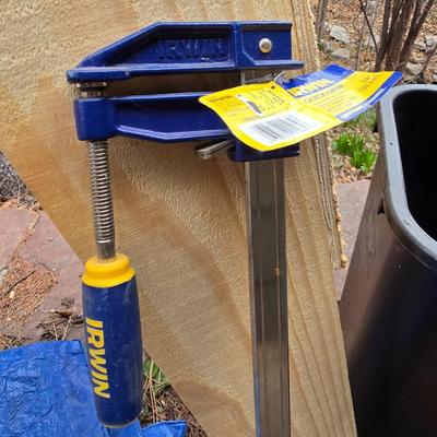 Wooden sawhorse, a blue tarp, Irwin clamp, and a trashcan