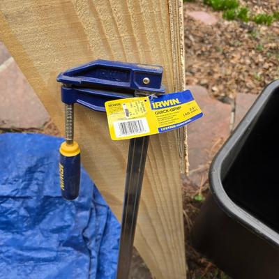 Wooden sawhorse, a blue tarp, Irwin clamp, and a trashcan