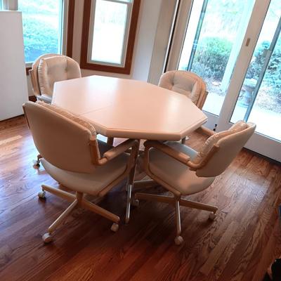 WHITE OCTAGON SHAPED TABLE WITH 4 WHITE VINYL CHAIRS ON CASTERS PLUS 1 LEAF
