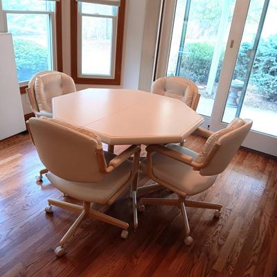 WHITE OCTAGON SHAPED TABLE WITH 4 WHITE VINYL CHAIRS ON CASTERS PLUS 1 LEAF