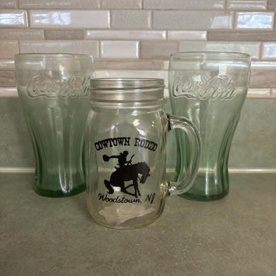 LOT 90: Glass Collection with Avocado Green Glass Mugs, Amber Glass Mug, Milk Glass, 25th Harley Davidson Mug, Coca-Cola Glasses, Cowtown...