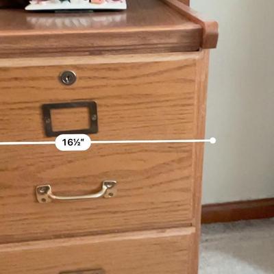 Sale Photo Thumbnail #17: Two-drawer wooden file cabinet constructed of oak with a natural finish. Features brass handles and a built-in locking mechanism for secure storage. Dimensions are approximately 18.5 inches in width, 25.5 inches in height, and 22 inches in depth. Suitable