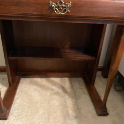 Sale Photo Thumbnail #46: A wooden roll-top desk featuring a tambour-style sliding top, a drawer with brass hardware, and a compartment with four small interior drawers for storage. Includes a matching wooden chair with a cushioned black seat. Desk shows visible wear. Measures 28 