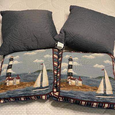 Sale Photo Thumbnail #58: Four decorative throw pillows featuring a nautical theme. Two pillows showcase a textured tapestry design depicting a lighthouse, sailboats, and ocean scenery, accented with striped edges. The reverse side of these pillows is solid navy blue. The other tw