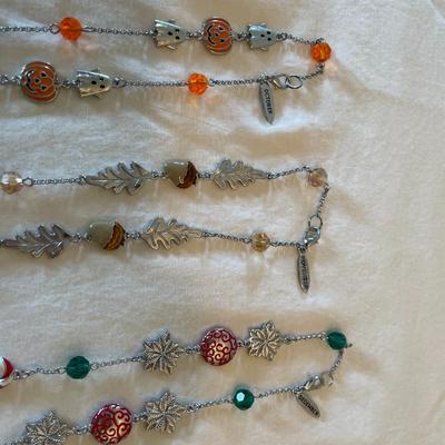 Sale Photo Thumbnail #88: A diverse collection of themed and seasonal necklace chains featuring a variety of charms and beads. Themes include seasonal elements such as Halloween, Christmas, and springtime, with charms such as pumpkins, bats, Christmas trees, candy canes, flowers, 