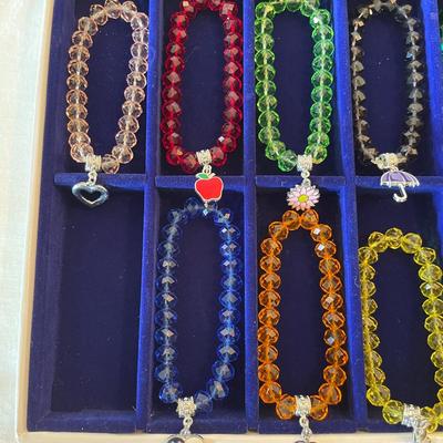 Sale Photo Thumbnail #119: 10 stretchable beaded bracelets in assorted colors including red, yellow, blue, green, and orange. Each bracelet features a unique decorative charm, such as a heart, apple, pumpkin, umbrella, and other themed designs. Comes in a fitted blue presentation t