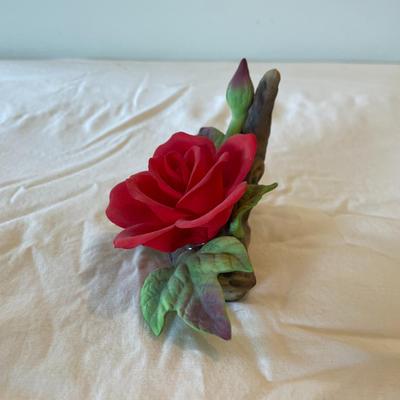Sale Photo Thumbnail #183: Handcrafted ceramic red rose figurine resting on a detailed log-style base, adorned with green leaves and a rosebud. Has felt pads for surface protection. Measures approximately 5 inches in length.