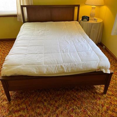Sale Photo Thumbnail #210: Full-size wooden bed frame featuring a solid headboard with rectangular cutouts on either side and a matching paneled footboard. The bed is constructed from wood with a warm brown finish and includes slatted wooden supports. The frame measures approximate