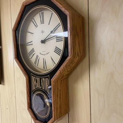 Sale Photo Thumbnail #375: Elgin wall clock with quartz movement and Westminster chime. Features an octagonal oak frame, with 'Regulator' text and an inset pendulum behind glass. The clock's face displays Roman numerals and measures approximately 13.5 inches in diameter, with the e